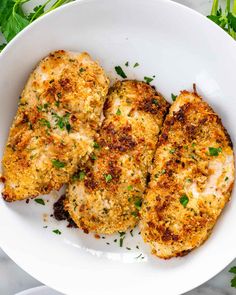 three pieces of chicken with parsley on top in a white bowl and garnished with parsley