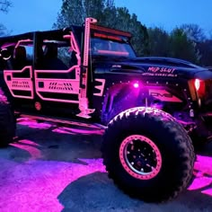 a pink jeep with big tires parked in front of some trees and bushes at night