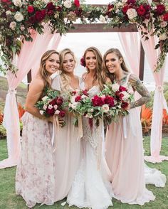 four bridesmaids pose for a photo in front of an arch decorated with red and white flowers