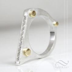 A bold minimalist ring, with a brushed finish, polished gold accents and a row of channel set stones. This ring will stack well with other rings, or can be worn alone. Makes a wonderful anniversary gift, or wedding ring. Made to order! Please allow about 1-2 weeks for your ring to be crafted. Features: ~All rings will feature 9 stones, all 2mm, round brilliant cut, channel set. ~All rings feature polished 18k yellow gold accent droplets on one side ~On the other side are 3 polished divots, direc Modern Channel Set Stackable Rings, Modern Formal Stackable Channel Set Rings, Modern Channel Set Diamond Promise Ring, Modern Sterling Silver Rings With Pave Setting, Modern Diamond Stackable Rings With Channel Set, Modern Sterling Silver Ring With Pave Setting, Modern Open Ring Jewelry With Single Cut Diamonds, Modern Channel Set Ring Jewelry, Modern Channel Set Diamond Ring