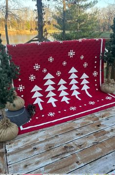 a red blanket with white trees on it sitting on a wooden deck next to potted plants