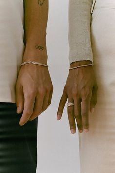 two people holding hands with tattoos on their arms and wristbands, both wearing rings