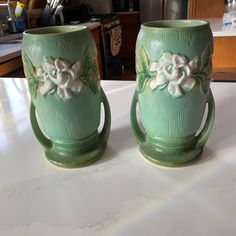 two green coffee mugs sitting on top of a white counter next to each other