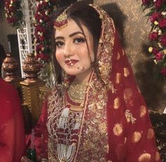 a woman wearing a red and gold bridal outfit in front of a floral arrangement