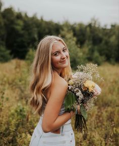 a woman standing in a field holding a bouquet of flowers