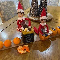 two elfs sitting on top of pumpkins in front of an orange peel basket