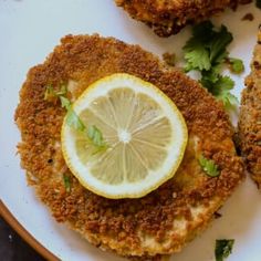 some fried food on a white plate with lemon wedges and garnishes