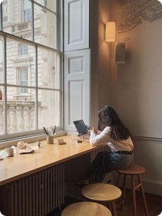 a woman sitting at a table with a laptop computer in front of a large window