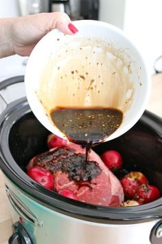 someone pouring sauce into a slow cooker filled with meat and potatoes for roasting