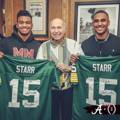 three men holding green jerseys in front of a wooden wall with framed photos on it