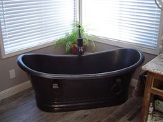 a black bath tub sitting in the middle of a bathroom next to a window with blinds