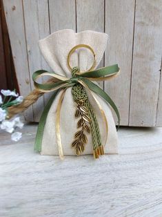 a white bag with a green ribbon tied around it and a gold leaf decoration on the front