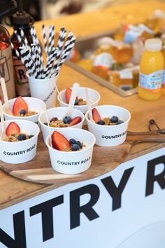 several cups with strawberries and blueberries in them on a tray next to a sign