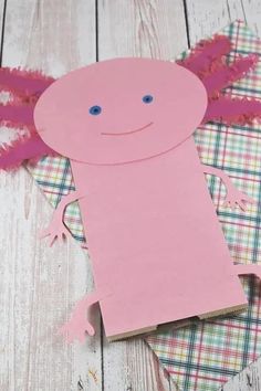 a paper cut out of a pink creature on top of a plaid tablecloth with scissors