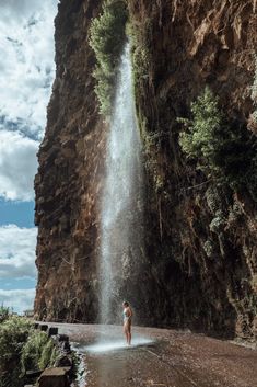 a person standing in front of a waterfall with water coming out of the side of it