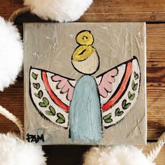 a painting on a piece of wood with white pom - poms around it