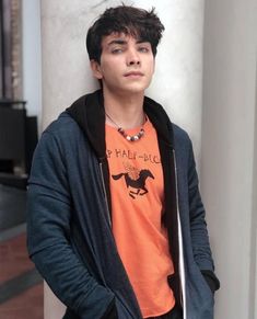 a young man leaning against a pillar wearing an orange shirt