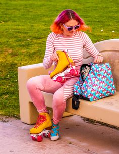 a woman with red hair sitting on a bench next to a bag and purse holding a pair of yellow boots