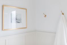 a bathroom with white walls and gold framed pictures on the wall next to a towel rack