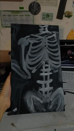 a person holding up a skeleton painting in front of a laptop