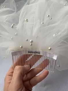 a person holding a hair comb with pearls on the top and white tulle around it