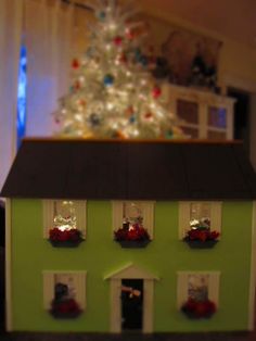 a doll house with christmas decorations on the windows and a small tree in the background