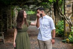 a man and woman standing next to each other on a path in the woods holding hands