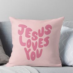 a pink pillow with the words jesus loves you written in pink on it, sitting on a couch