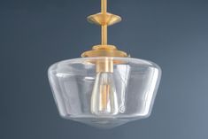 a clear glass light fixture hanging from a gold colored chandelier against a blue wall