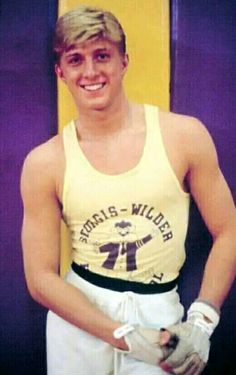 a man in yellow shirt and white shorts standing next to purple wall with baseball glove