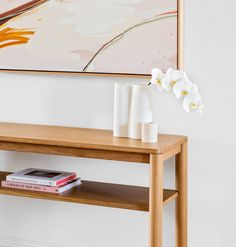 a wooden table topped with a white vase filled with flowers next to a painting on the wall