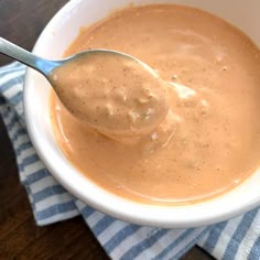 a spoon in a white bowl on top of a blue and white striped napkin with a brown sauce