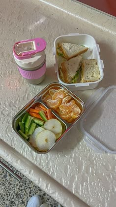 there is a lunch box with sandwiches and fruit on the table next to a cup of coffee