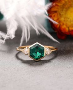 an emerald and diamond ring sitting on top of a table next to feather quill