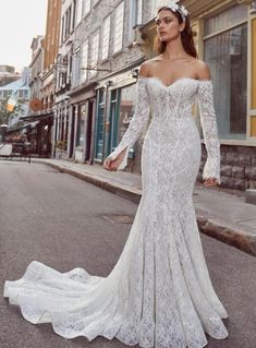 a woman in a white wedding dress standing on the street with her arms outstretched and looking off to the side