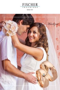 a bride and groom embracing each other in front of a pink wall with their wedding rings