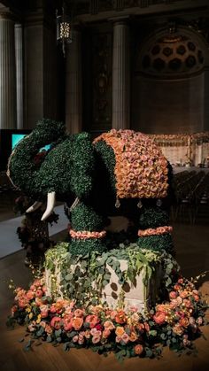 an elephant made out of flowers and greenery on display in a room with columns