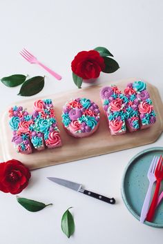 three decorated cupcakes sitting on top of a tray next to scissors and flowers