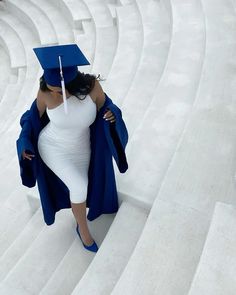 a woman in white dress and blue graduation cap walking up steps with an umbrella over her head