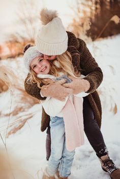 a man and woman hugging in the snow with their arms around each other while wearing winter clothes