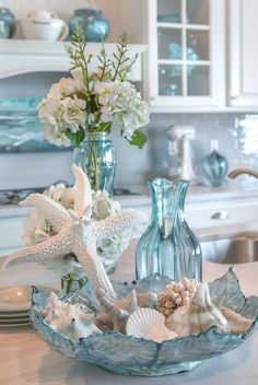 two vases filled with flowers and seashells sit on a kitchen counter top