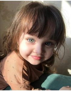 a close up of a child with blue eyes and brown shirt smiling at the camera