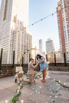 a man kneeling down next to a woman on top of a roof with candles in the air