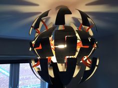 a lamp that is hanging from the ceiling in front of a window with an orange and black design on it