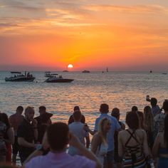 a group of people standing on top of a beach next to the ocean at sunset