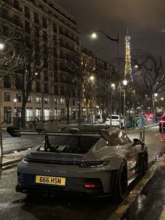 a grey sports car parked on the side of a street next to a tall building