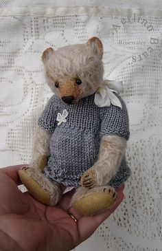 a small teddy bear in a sweater is held by someone's hand on a lace tablecloth