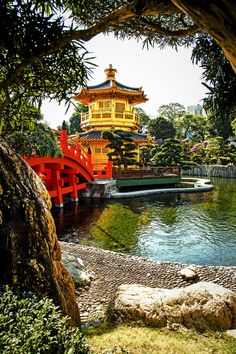 a red and yellow bridge over water next to a lush green forest filled with trees