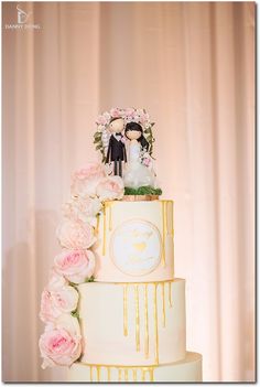 the wedding cake is decorated with pink flowers and figurines on top, along with gold drips