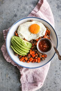 a plate with eggs, carrots and avocado on it next to a spoon